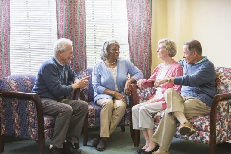 Four elderly people sit together in a living room, engaged in conversation.
